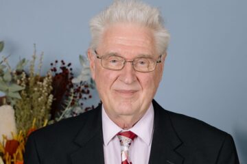 A white haired man, wearing glasses.