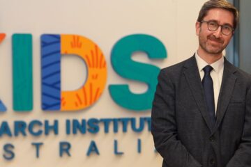 A suited man next to a sign for The Kids Research Institute Australia