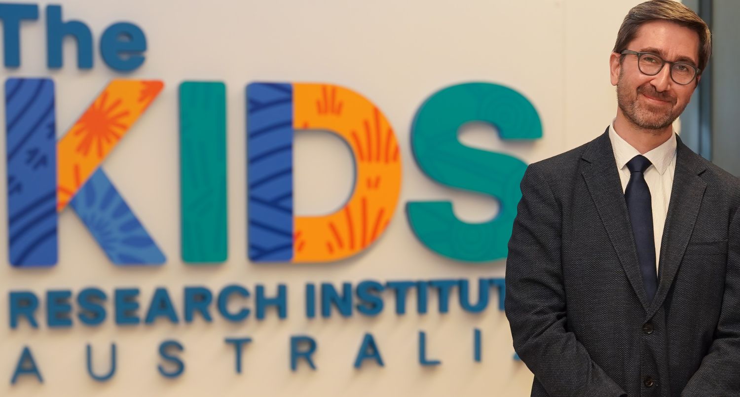 A suited man next to a sign for The Kids Research Institute Australia