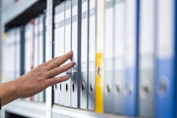 A hand moving across rows of files on a shelf.