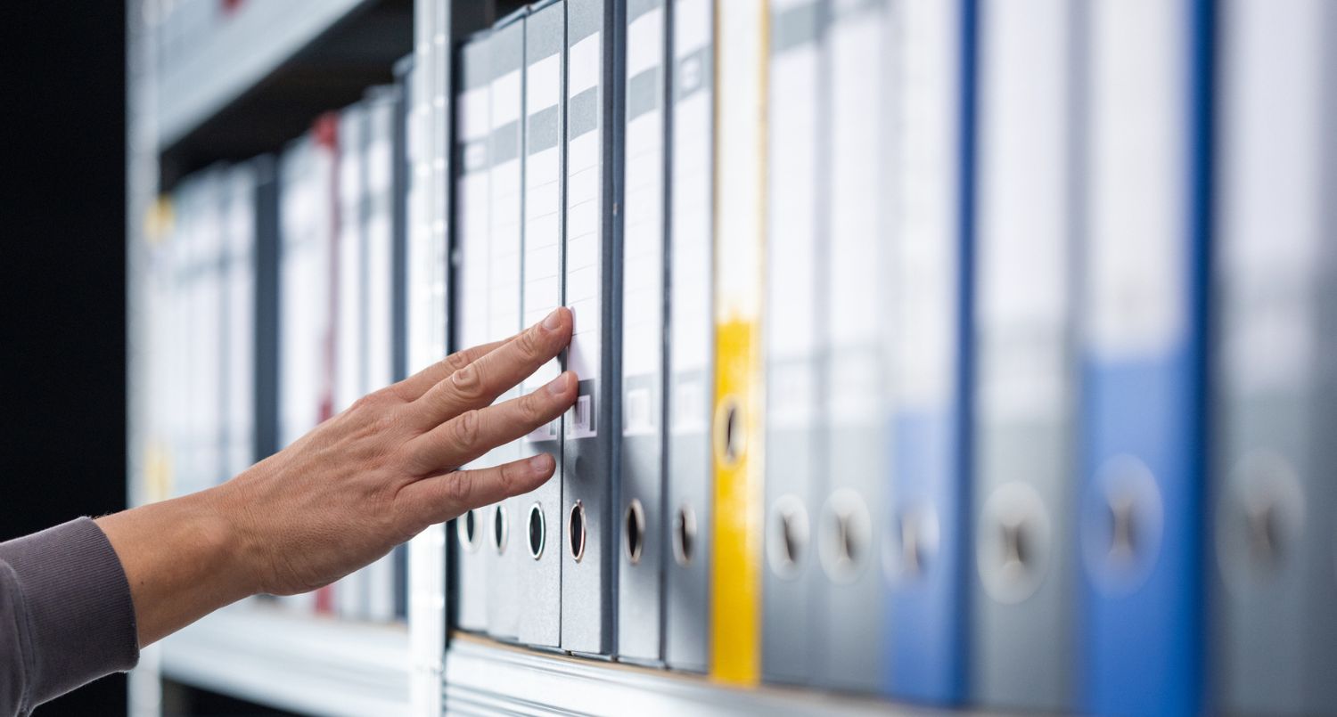 A hand moving across rows of files on a shelf.